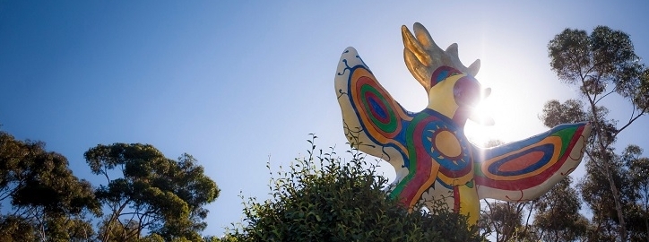 The colorful Sun God statue, with green trees and a blue sunny sky in the backdrop